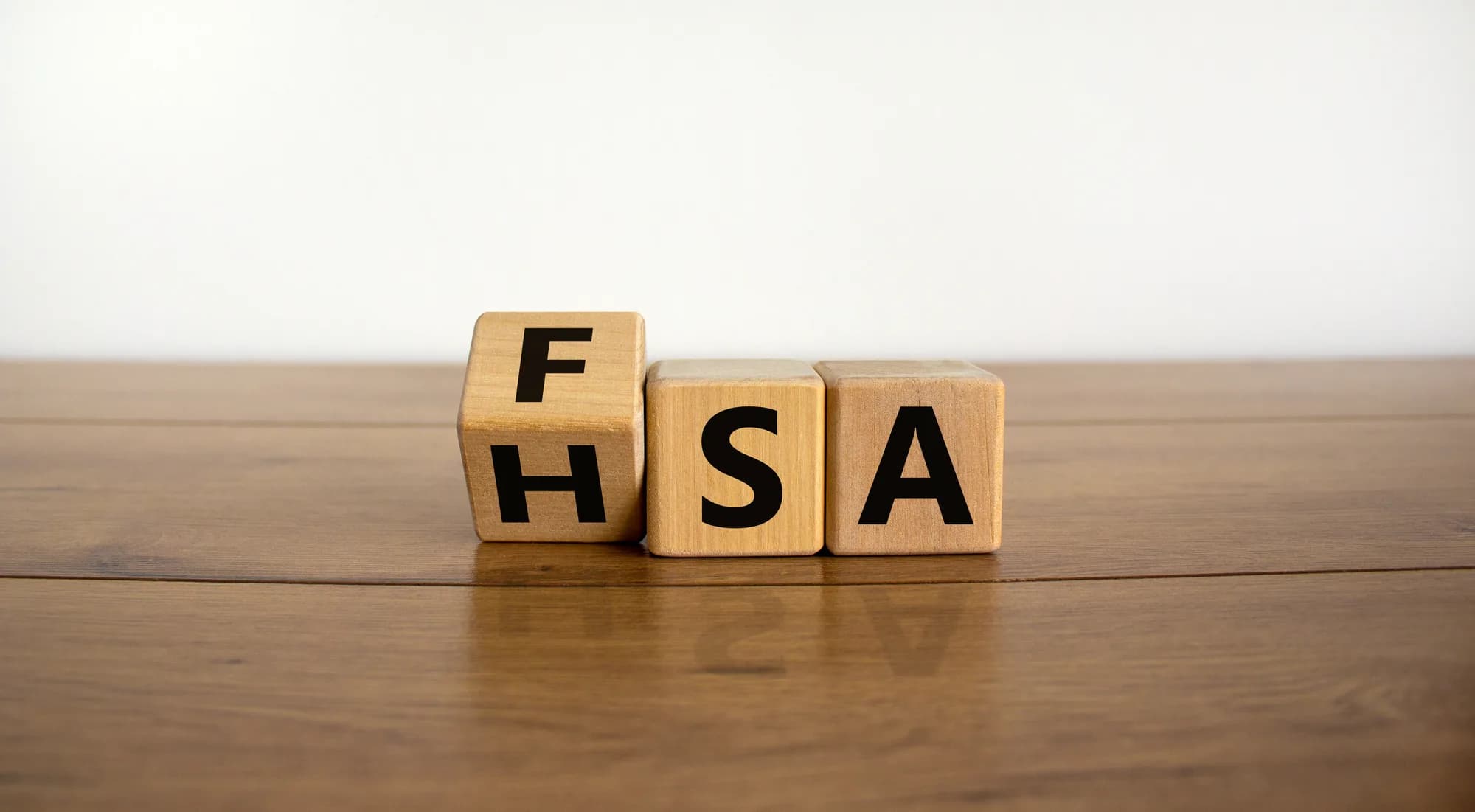 Wooden blocks turning the letters FSA into HSA on a desk